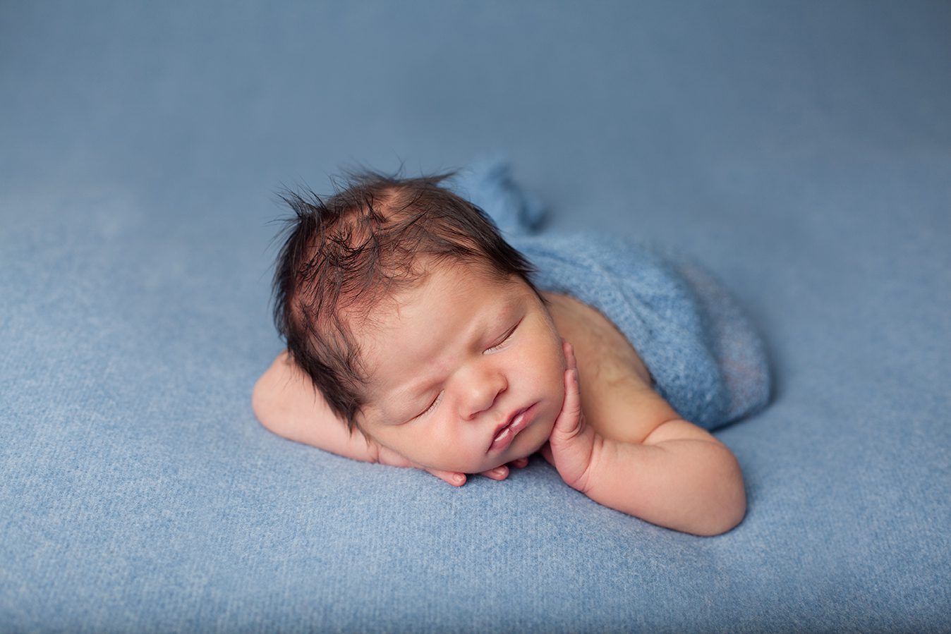 newborn boy with hand on face on tummy bean bag pose