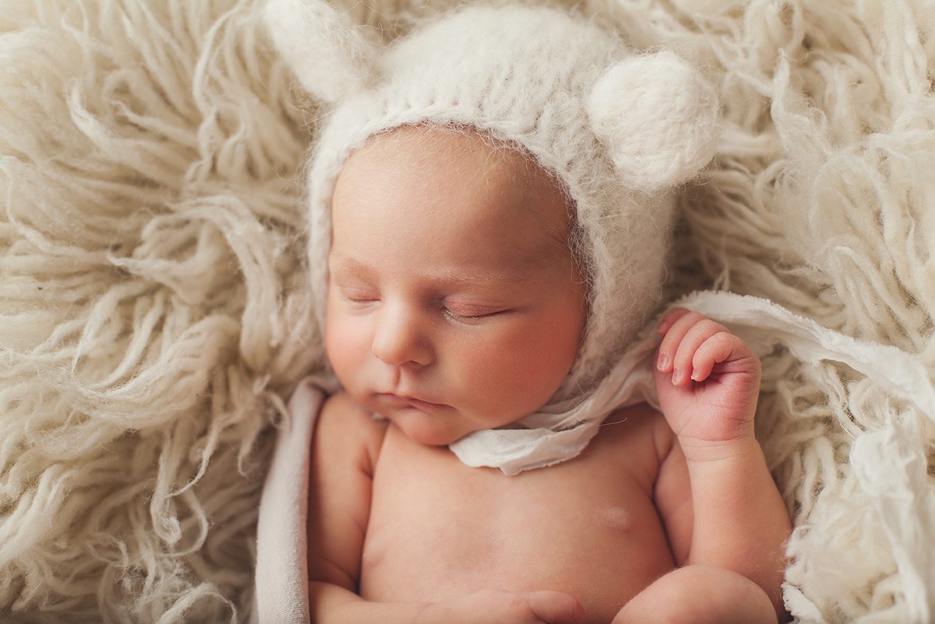 newborn girl with alpaca cream teddy bear hat on flokati