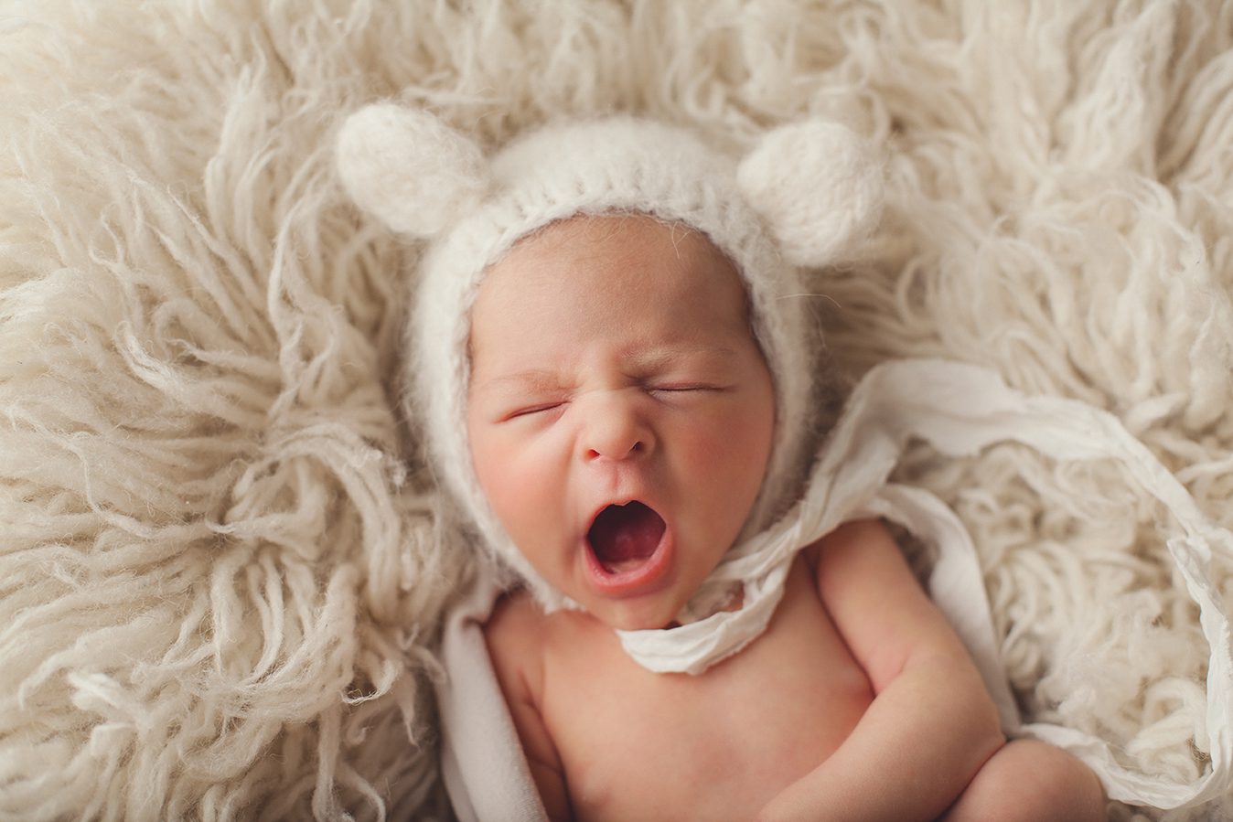 yawning newborn girl with alpaca cream teddy bear hat