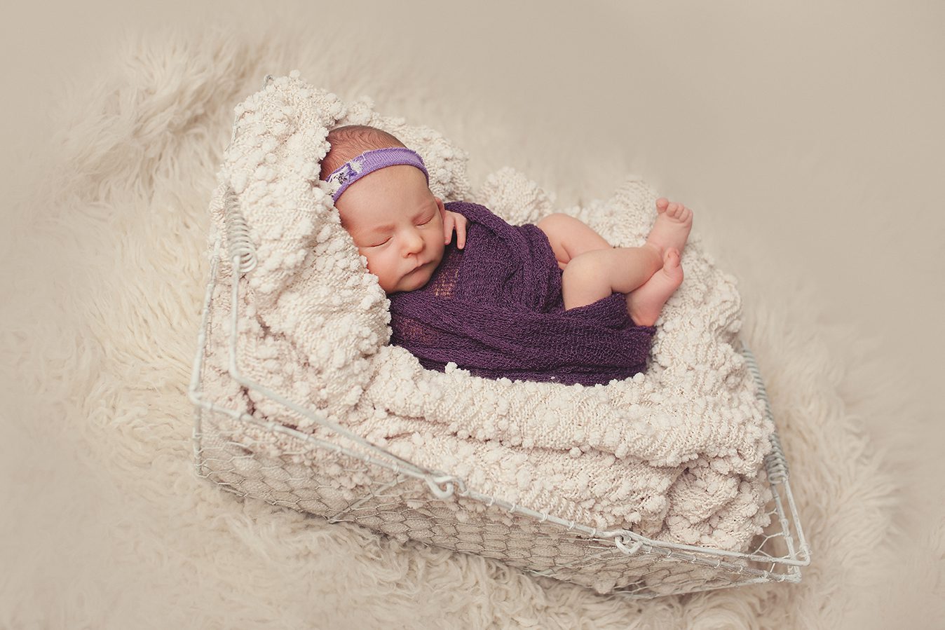 side view of newborn girl wrapped in purple on basket