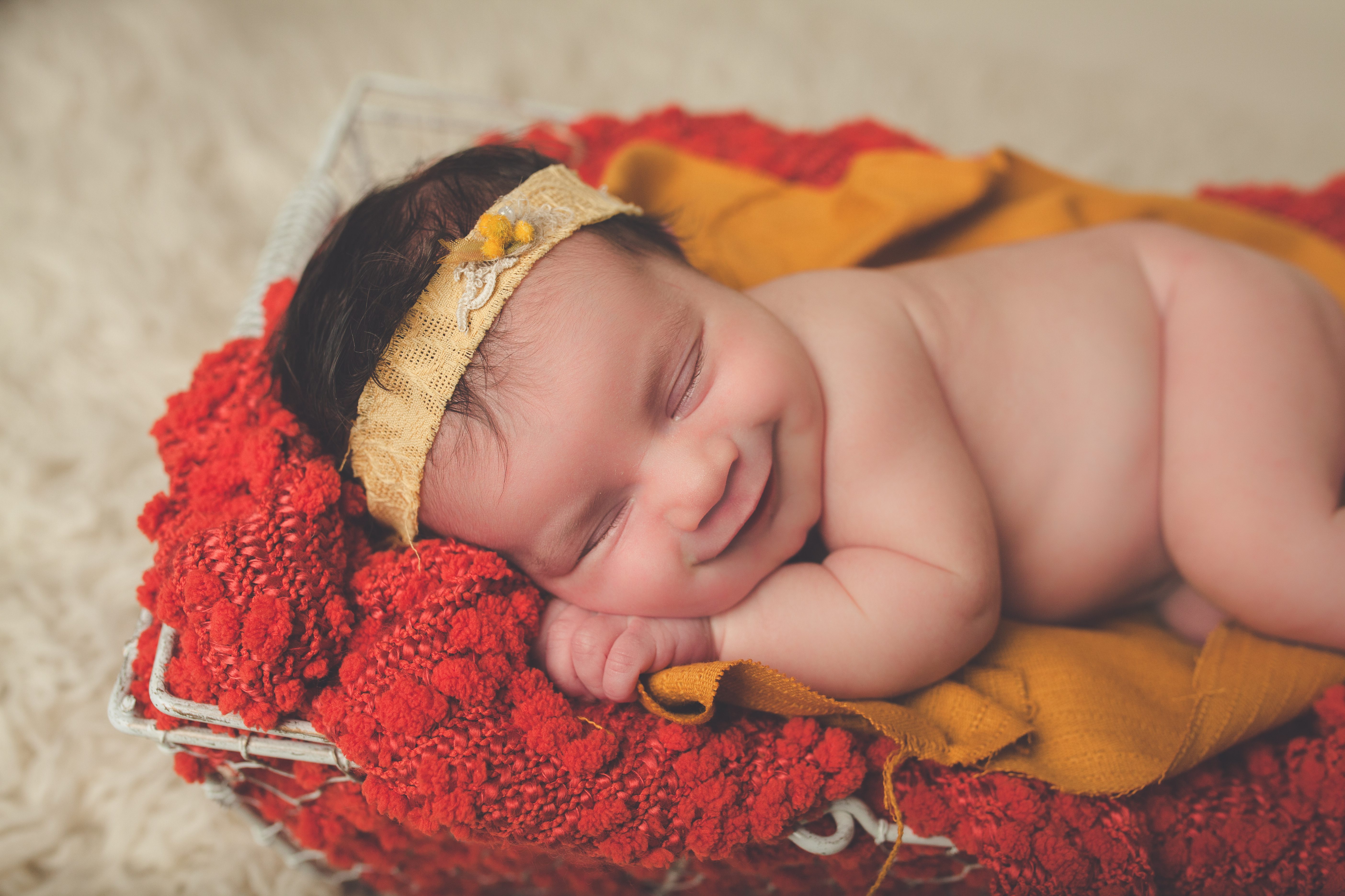 newborn posed smiling in basket on red blanket