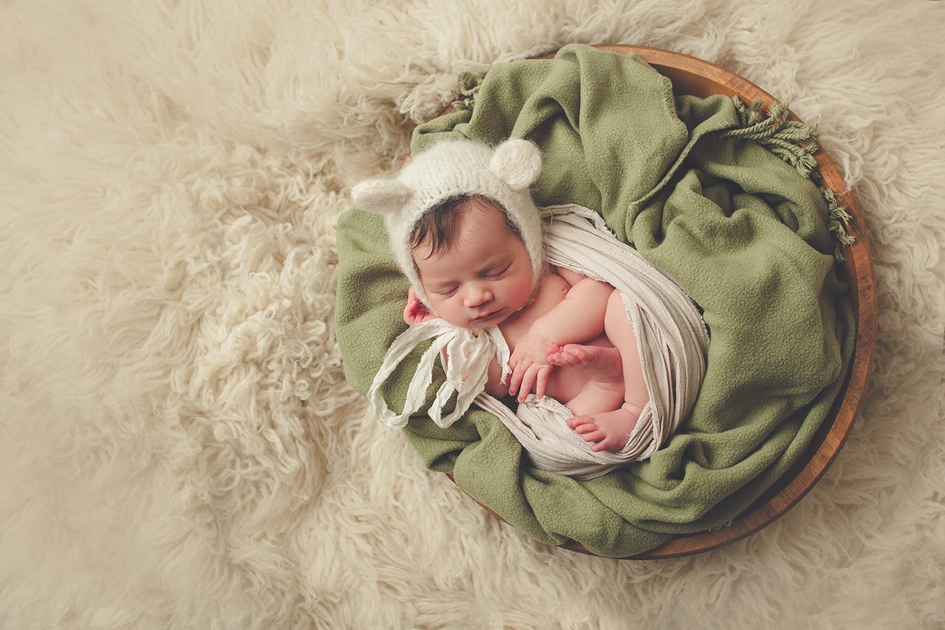posed newborn photography with green blanket in antique bowl