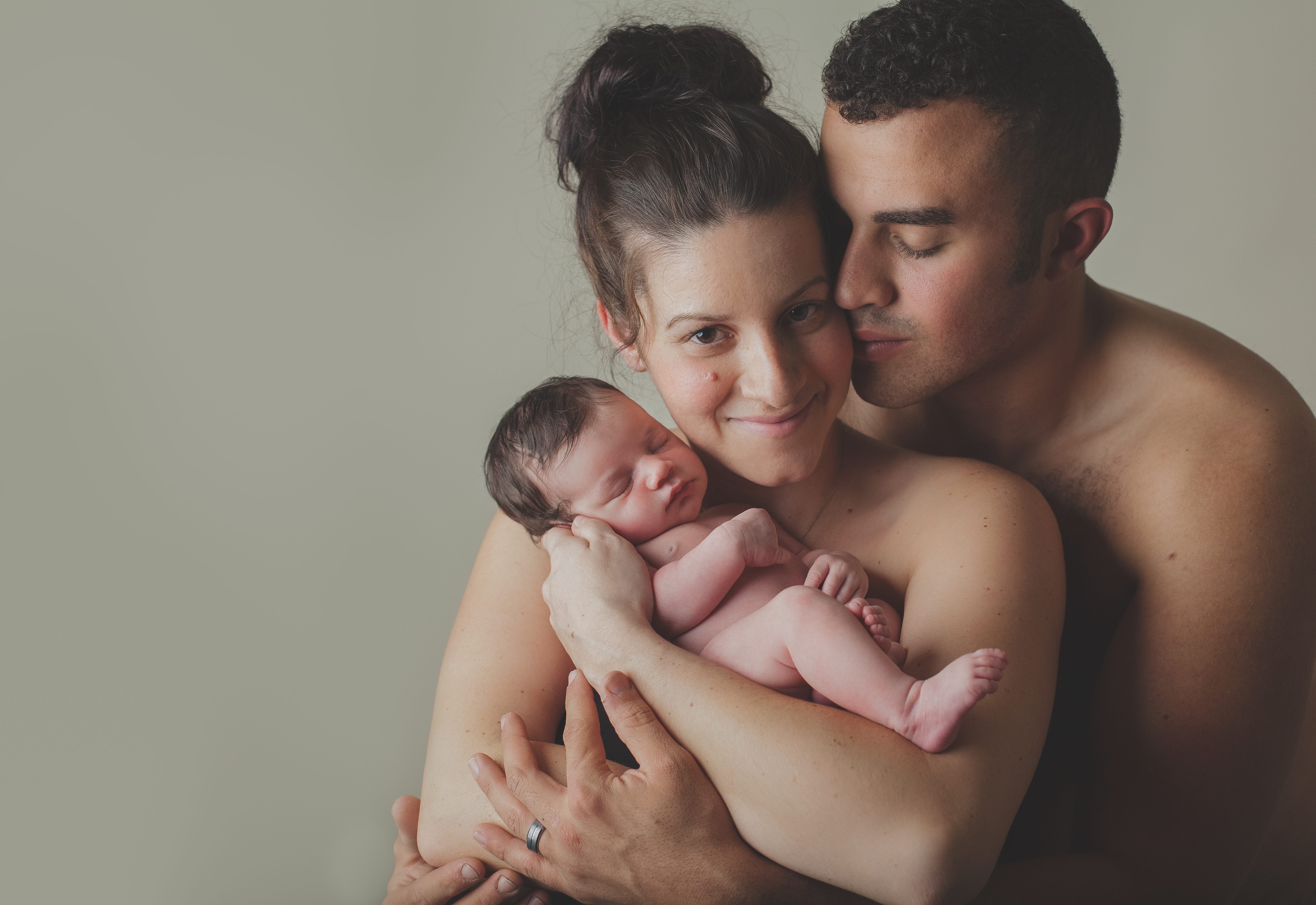 family pose of newborn in daddy's arms with daddy kissing mommy