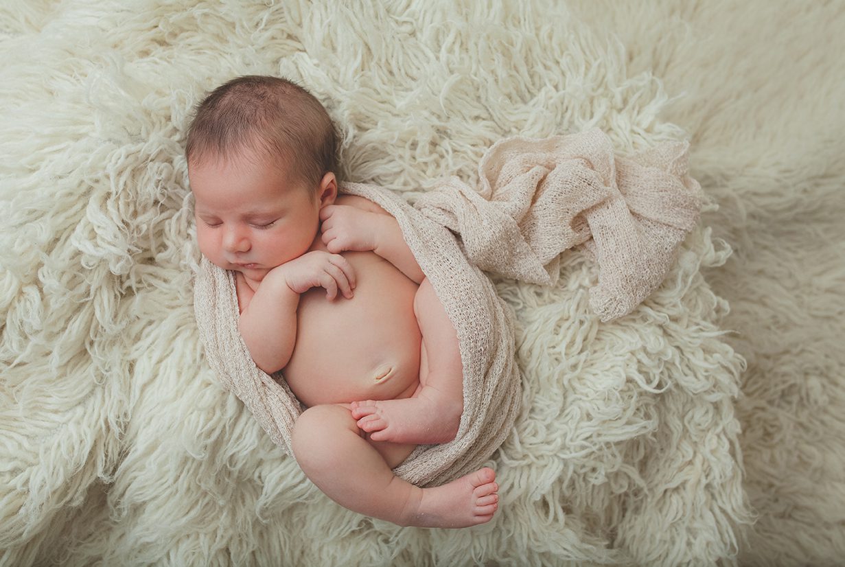 top view of newborn girl in wrap on flokati