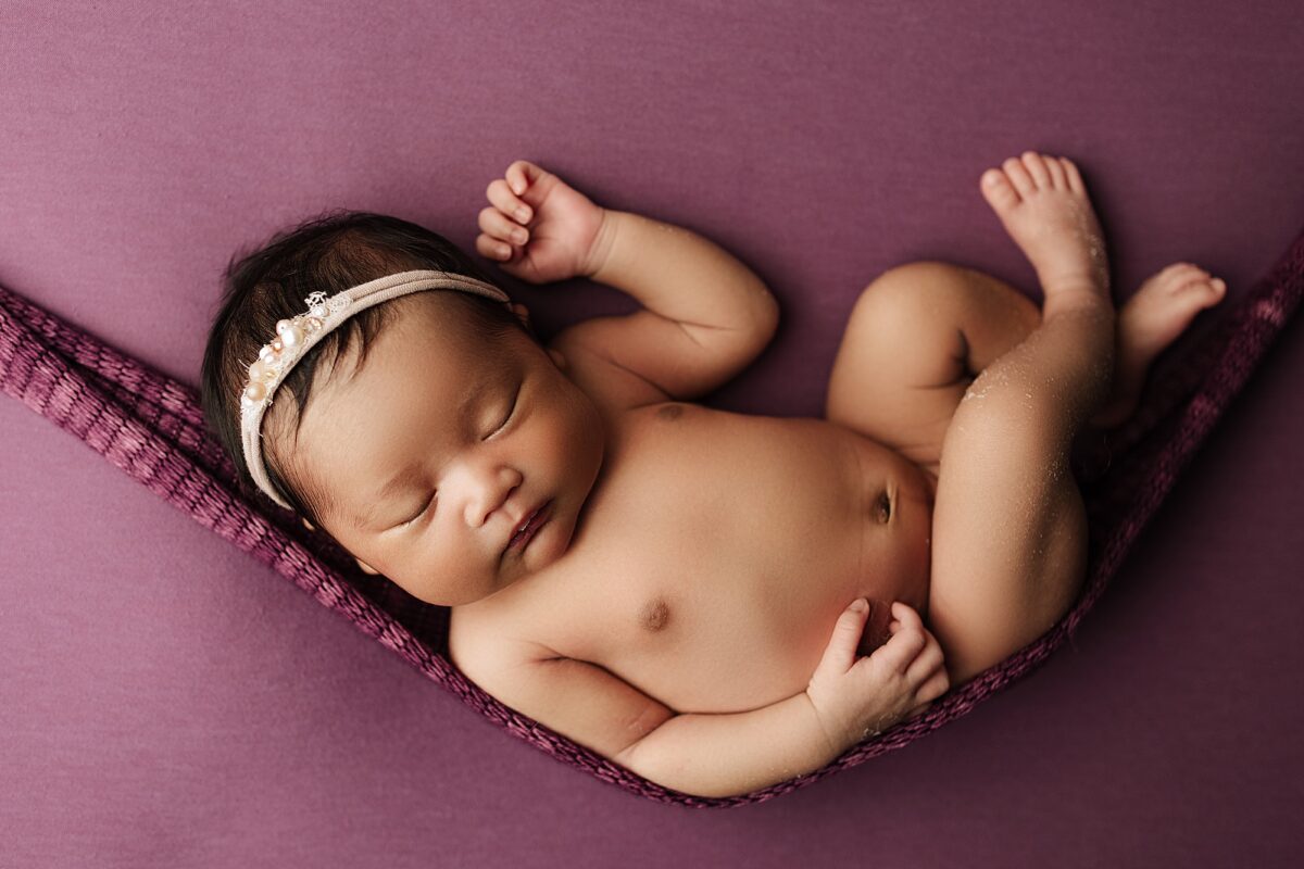 hammock pose, newborn girl posed on purple fabric